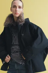 Trench corto de corte recto con capucha y cuello desmontable efecto pelo. Presenta cierre frontal con botones, bolsillos laterales y mangas largas con trabillas en los puños.