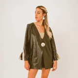 Blazer de cuero sintético color verde militar, con cuello en V profundo, cierre frontal con un botón grande en contraste y mangas largas con puños abiertos que dejan ver apliques en tonos beige y marrón.