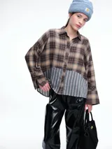 Camisa de corte relajado con diseño combinado. La parte superior presenta un estampado a cuadros en tonos marrones y negros, mientras que la parte inferior destaca por un panel de rayas verticales en color bordó. Cuenta con cierre frontal de botones y mangas largas.