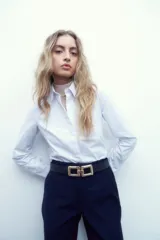 Camisa de corte clásico, color blanco, con cuello camisero, cierre frontal de botones y mangas largas con puños abotonados.
