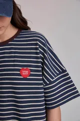 Remera oversize a rayas horizontales en tonos bordó y blanco, con cuello redondo verde oscuro y un pequeño parche bordado en forma de corazón en el pecho.
