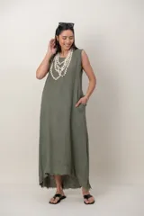 Vestido largo de lino color verde militar, sin mangas, con cuello redondo y bolsillos laterales. Presenta detalles desflecados en las sisas y en el dobladillo asimétrico.