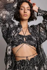 Top corto negro con estampado floral blanco, con parte delantera ajustable mediante cordones y fruncido. Tirantes elásticos y botones metálicos en la espalda.