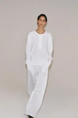 Camiseta blanca de manga larga y corte regular fit, confeccionada en mezcla de algodón y lino. Presenta cuello panadero con cierre frontal de botones y bajo recto.
