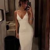 Vestido largo color marfil de corte sirena, con escote en V pronunciado, tirantes finos y aplicaciones de pedrería y tachas metálicas distribuidas en el frente.