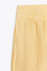 Short de tiro medio de lino 100%, color amarillo claro. Presenta cintura elástica, cierre frontal con botones y bolsillos laterales ocultos en costura y de plastrón en la espalda. El bajo tiene aberturas laterales.