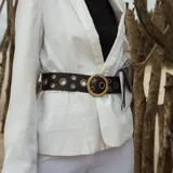 Cinturón de cuero negro con hebilla circular dorada y ojales metálicos.