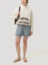 Buzo color beige con cierre frontal parcial y cuello alto. Presenta un bolsillo tipo canguro con diseño tejido a rayas horizontales en tonos marrón, beige y blanco.