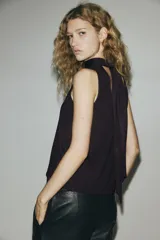Top sin mangas de punto fino suave, color marrón oscuro, con cuello alto drapeado y detalle decorativo efecto pañuelo.