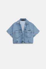 Camisa corta de denim en color azul claro, con cuello solapa, escote en V y manga corta. Presenta bolsillos delanteros de parche con solapa y cierre frontal de botones metálicos.