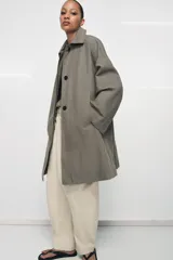 Trench oversize de Zara Woman Collection, confeccionado en hilatura de algodón. Presenta cuello solapa, manga larga, bolsillos delanteros y cierre frontal con botones ocultos bajo solapa.