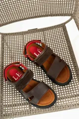 Sandalias de cuero marrón con diseño de tiras anchas y ajuste mediante velcro. Presentan una plantilla acolchada color tostado con detalles en rojo y una suela de goma negra con plataforma dentada.