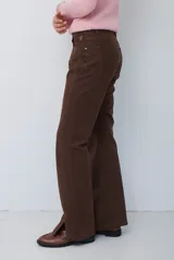 Pantalón tipo jean de corte recto y tiro medio, color burdeos, con costuras a tono y abertura lateral en el ruedo.