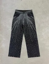 Jeans de corte recto y tiro alto, confeccionados en denim color negro, con diseño aplicado de pedrería y tachas brillantes que forman un patrón radiante desde la cintura y los bolsillos hacia las piernas.