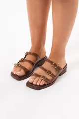 Sandalia de cuero marrón con diseño de tres tiras con hebillas metálicas doradas regulables y punta cuadrada.