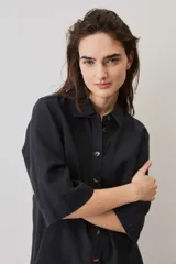 Camisa negra de manga corta, con cuello camisero, cierre frontal de botones y un bolsillo aplicado en el pecho.