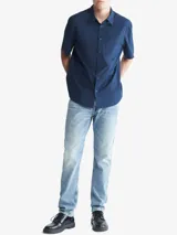 Camisa azul marino de manga corta, con cuello clásico, cierre frontal con botones, bolsillo de parche en el pecho izquierdo y logo CK bordado en el bolsillo.