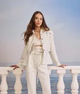 Chaqueta corta color blanco, con cuello camisero, cierre frontal con botones metálicos y apliques de tachas metálicas en los hombros.
