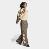 Pantalón deportivo Adidas de corte holgado, color marrón con detalles en beige en la parte inferior de las piernas. Presenta cintura elástica con cordón de ajuste y logo de la marca bordado en el muslo.