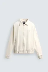 Cazadora de algodón color crema, corte regular fit, con cuello solapa, cierre frontal de cremallera y puños y bajo elásticos. Presenta bordado a tono en el delantero y espalda, y un parche combinado a contraste en la espalda.