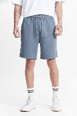 Short de felpa color azul grisáceo, sin frisa, con cintura elástica y cordón ajustable. Presenta un pequeño logo estampado en la parte inferior de una de las piernas.