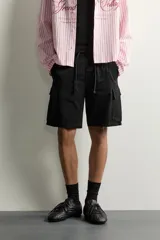 Bermuda cargo color negro de corte relaxed fit, confeccionada en tejido de algodón con elasticidad y efecto lavado. Cuenta con cintura elástica ajustable con cordón, bolsillos frontales y bolsillos laterales tipo cargo con solapa en las perneras.