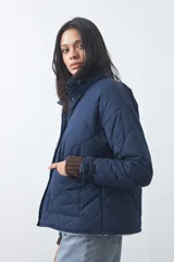 Campera acolchada de nylon color negro, con cuello alto, cierre frontal y botones a presión. Presenta un diseño de rombos y forro interior suave.