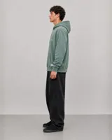 Canguro con capucha de color verde con efecto lavado, diseño de corte holgado, bolsillo frontal tipo canguro, cordones ajustables y logo estampado en el pecho.