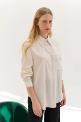 Camisa color crema de lyocell con cuello clásico, cierre frontal con botones y bolsillo de parche en el pecho. Presenta pespuntes a contraste en cuello, bolsillo, puños y tapeta.
