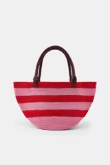 Bolso tipo cesto de yute con diseño de rayas horizontales en tonos rojo y rosado, asas de mano de cuero en color marrón oscuro y base redondeada.