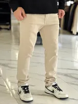 Pantalón de jean color beige, de corte regular y estilo chupín.