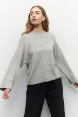 Sweater de tejido de punto color gris melange, con cuello redondo y diseño de franjas horizontales en relieve. Presenta mangas largas acampanadas y un corte holgado.