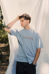 Remera de jersey lavado color azul claro, de corte holgado y cuello redondo, con bordado frontal en color rojo.