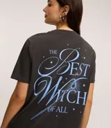 Remera de algodón color gris oscuro (efecto desteñido/vintage) con estampa frontal inspirada en el personaje Glinda, el Hada Buena, de la película Wicked. La estampa incluye el texto "SPARKLE LIKE GLINDA WICKED" y una ilustración de Glinda con su varita mágica.