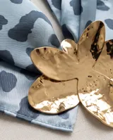 Pañuelo de seda celeste con estampado animal print azul y un dije metálico dorado en forma de flor que sujeta la prenda.
