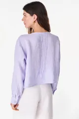 Camisa blanca de lino italiano, de manga larga, escote en V y cierre frontal con múltiples botones y detalles de alforzas.