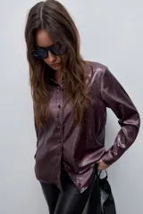 Camisa blanca de calce relajado con acabado satinado y brillo sutil, cuello clásico, cierre frontal con botones y mangas largas con puños.