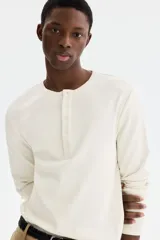 Remera de manga larga en tejido acanalado de algodón, color blanco, con cuello panadero redondo y tapeta corta con botones de ajuste. Corte slim fit que se ajusta a la silueta.