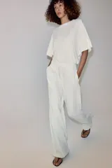 Pantalón wide leg de tiro medio, color blanco con diseño de rayas diplomáticas a contraste, bolsillos laterales y de vivo en la espalda, pinzas en el delantero y cierre frontal con cremallera, botón y ganchos metálicos.