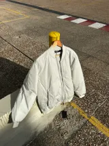 Campera bomber color crudo de nylon con cierre frontal y bolsillos laterales.