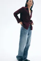 Blusa de manga larga color borgoña, con cuello clásico y escote en V con botones frontales. La tela tiene un acabado satinado y el bajo es redondeado.