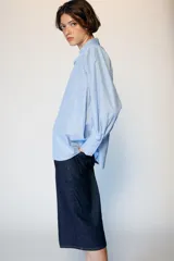 Camisa de manga larga con cuello solapa y hombreras. Presenta un diseño de rayas verticales en tonos azul y blanco, con cierre frontal de botones y puños anchos.