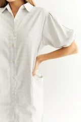 Vestido camisero midi de lino a rayas verticales grises y blancas, con cuello camisero, mangas cortas abullonadas, cierre frontal con botones y bolsillos laterales.