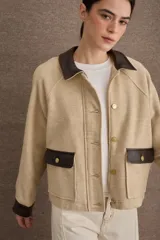 Campera corta de paño color marrón con detalles en cuero sintético al tono en cuello, puños y solapas de bolsillos. Presenta cierre frontal con botones metálicos dorados y dos bolsillos frontales tipo cargo.