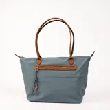 Bolso tipo tote bag color gris azulado con detalles en marrón. Tiene doble asa de hombro marrón, cierre superior y bolsillo frontal con cierre.