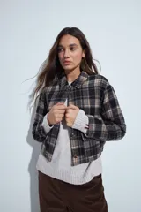 Campera de paño con diseño de cuadros en tonos negro, gris y beige. Presenta cuello camisero, cierre frontal con botones y corte corto.