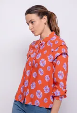 Camisa naranja con estampado de flores lilas, de manga larga con botones de plástico y detalle de alforzas en hombros.