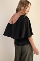 Top negro con diseño asimétrico de un solo hombro y manga tipo capa fluida. Confeccionado en tela ligera y suave, presenta un corte elegante que se ajusta al cuerpo.