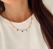 Gargantilla de cadena fina en acero quirúrgico dorado, con dijes colgantes de piedras de colores en diversas formas y tamaños.