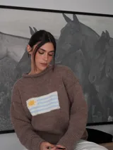 Sweater tejido a mano de color marrón, con diseño de la bandera de Uruguay en el frente. Presenta un calce relajado, cuello redondo y mangas largas con terminaciones simples.